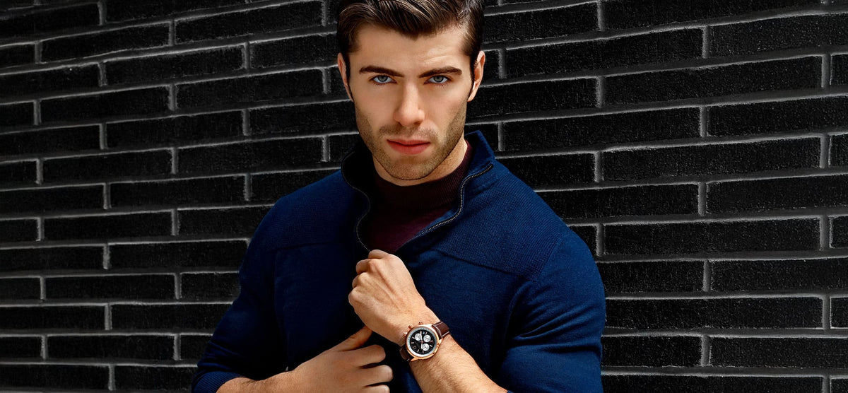 Man wearing a blue coat and watch against a dark brick wall