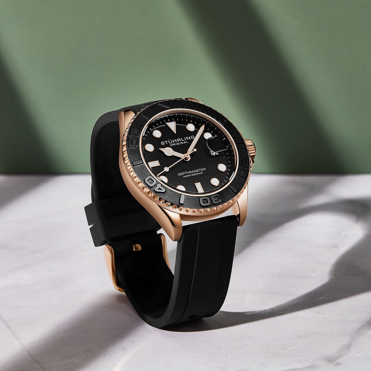 Watch with black strap and rose gold case on a light surface with green background