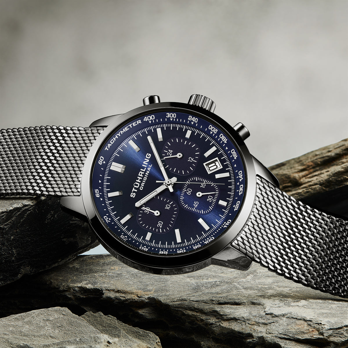 Stuhrling watch with blue face and silver mesh band on a stone surface